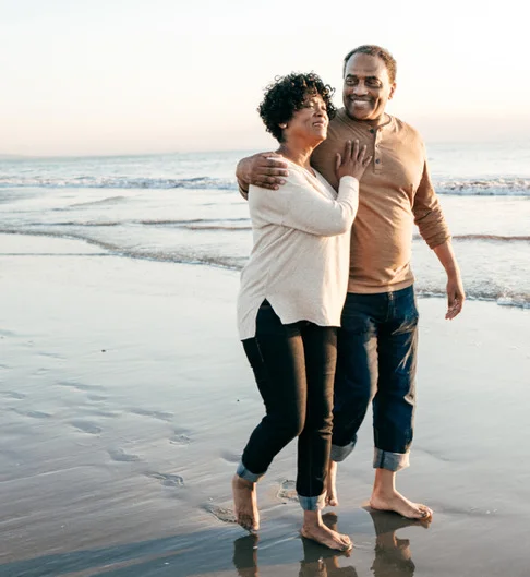 an elderly couple walks along the beach